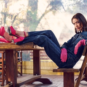 Puede incluir: Una mujer con una chaqueta vaquera y pantalones vaqueros se sienta en un banco de madera con las piernas apoyadas en una mesa de madera. Lleva tacones de plataforma rosa y guantes rosas.