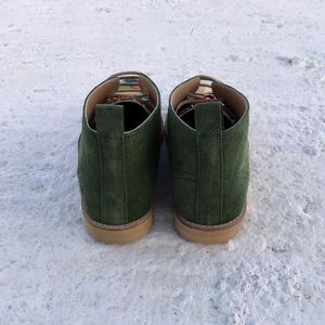 May include: A pair of dark green suede ankle boots with a colourful patterned trim around the top of the boot.