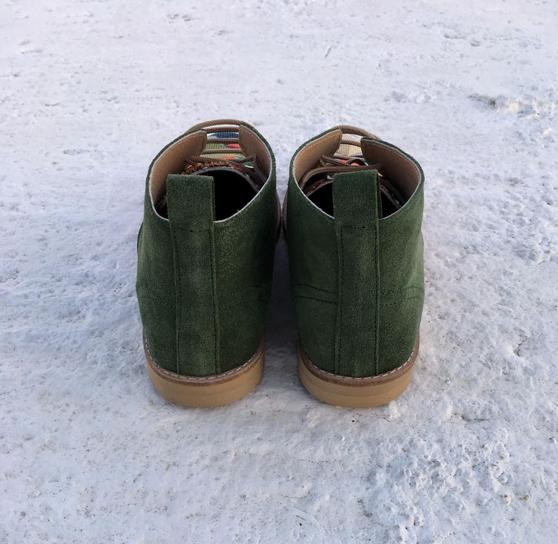 May include: A pair of dark green suede ankle boots with a colourful patterned trim around the top of the boot.