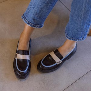 May include: A pair of black leather loafers with a light blue and beige trim. The loafers have a rounded toe and a thick sole.