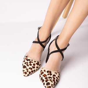 May include: A pair of black and brown leopard print heeled shoes with criss-cross straps.