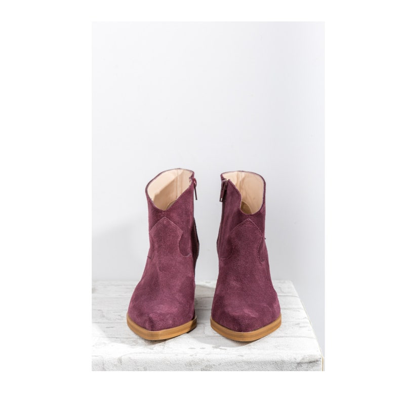 Pu&ograve; includere: Un paio di stivaletti in suede bordeaux con punta a punta e cerniera laterale.