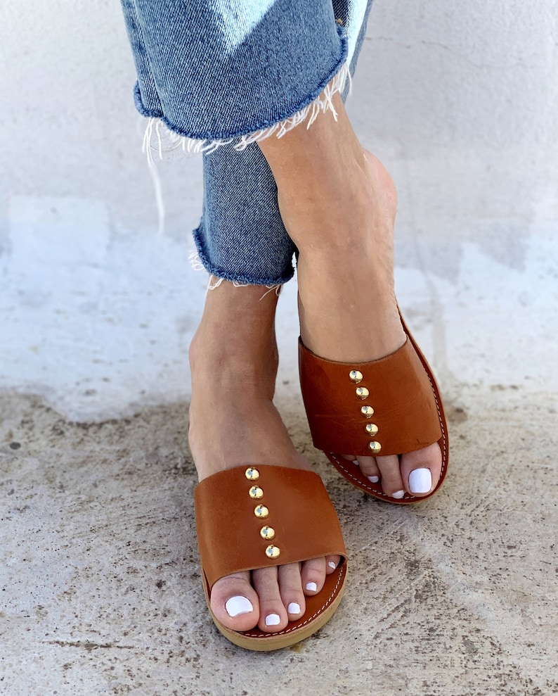May include: A pair of brown leather sandals with gold studs. The sandals have a simple design and are perfect for summer.