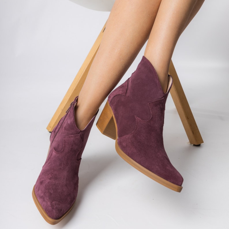 Pu&ograve; includere: Un paio di stivaletti in suede bordeaux con punta a punta e tacco a blocco. Gli stivaletti hanno una cerniera all'interno della caviglia.