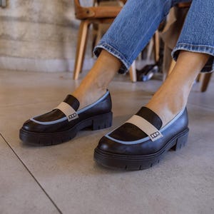 May include: Black leather loafers with a blue and beige trim and a thick sole. The loafers have a small logo on the side.