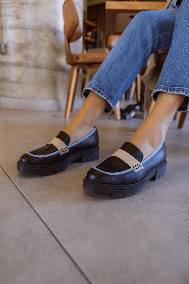 May include: Black leather loafers with a blue and beige trim and a thick sole. The loafers have a small logo on the side.