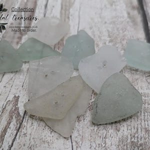 May include: A collection of sea glass pieces in various shapes and sizes. The glass is primarily pale green and clear, with a frosted appearance. The pieces are scattered on a light-colored wooden surface. Text on the image reads "Collection Tidal treasures."