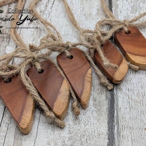 May include: Five wooden ornaments with a natural finish, each with a hole for hanging and tied with twine. The ornaments are a mix of light and dark wood tones. The text "Collection Fireside Yule" is visible in the upper left corner.