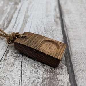 May include: A wooden pendant with a small hole in the centre, attached to a brown twine cord. The pendant is made of dark brown wood with a natural grain pattern.