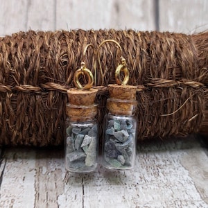 May include: A pair of gold earrings with small glass bottles filled with green and gray stones. The bottles have cork stoppers and are attached to gold hooks.