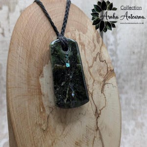May include: A green stone pendant with a black cord necklace. The pendant has a vertical line of iridescent abalone shell inlay.  Collection Aroha Aotearoa. www.kerrieowenarts.co.uk