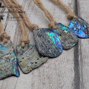 May include: A selection of tumbled Abalone shell pendants, displaying iridescent colours of blue, green, and silver. Each shell is unique, suspended from a natural rope cord. Part of the "Ocean edition" collection.