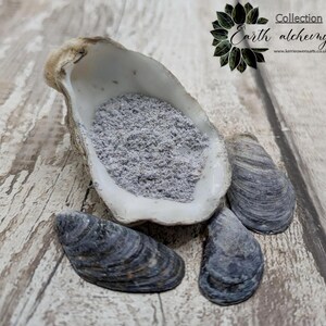 May include: A white seashell filled with a light purple powder. Three dark grey seashells are on a light wood surface. The text "Collection Earth alchemy. www.kerriewensarts.co.uk" is in the upper right corner of the image.