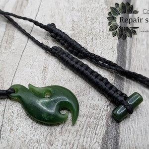 May include: A dark green jade pendant in a hook shape, with a black cord, and a matching jade toggle. The image also shows a black braided cord. Text in the image reads "Collection Repair services".