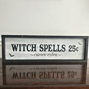Puede incluir: Un letrero enmarcado en negro con pintura blanca y letras negras que dice "Witch Spells 25&cent; ~curses extra~" con una silueta de murci&eacute;lago negro a cada lado del texto.