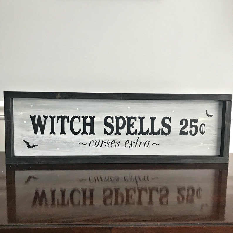 Puede incluir: Un letrero enmarcado en negro con pintura blanca y letras negras que dice "Witch Spells 25&cent; ~curses extra~" con una silueta de murci&eacute;lago negro a cada lado del texto.