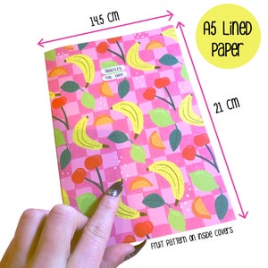 May include: A5 lined paper notebook with a pink and white checkered background and a fruit pattern on the inside covers. The fruit pattern includes bananas, lemons, oranges, and cherries. The notebook measures 14.5 inches by 21 inches. The text "Squeeze the Day!" is printed on the front cover.