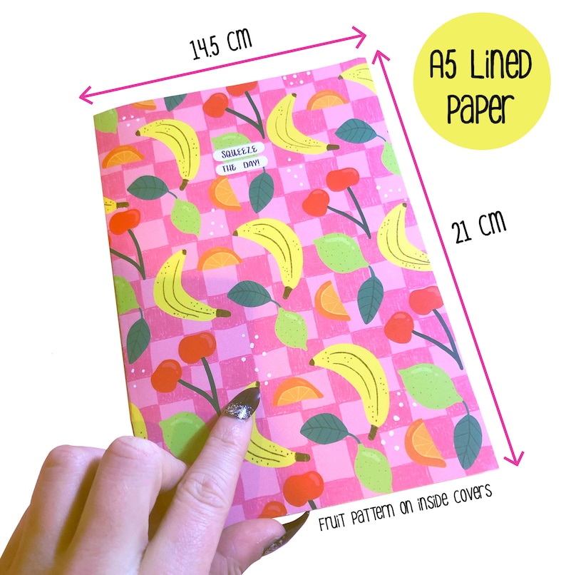 May include: A5 lined paper notebook with a pink and white checkered background and a fruit pattern on the inside covers. The fruit pattern includes bananas, lemons, oranges, and cherries. The notebook measures 14.5 inches by 21 inches. The text "Squeeze the Day!" is printed on the front cover.