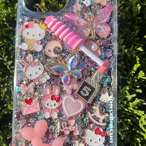 May include: Clear phone case decorated with pink and iridescent glitter, Hello Kitty, butterflies, and other charms. A pink lollipop and lipstick charm are also included. The word "Sweet" is written on the case.