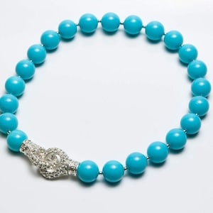 Può includere: Una collana di perle blu turchese con una chiusura argentata tempestata di strass trasparenti.