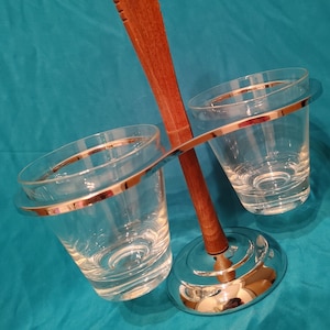 May include: A chrome and wood double glass holder with a wooden handle. The holder has two clear glass cups with silver rims.
