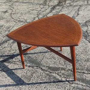 May include: A triangular wooden table with a dark brown finish and a simple, modern design. The table has three legs that extend from the corners of the triangular top.