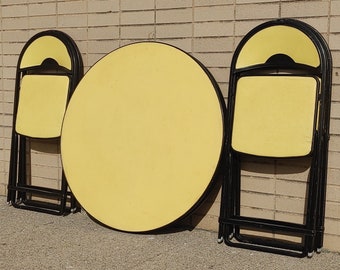 May include: A set of three yellow folding chairs and a round yellow table with black metal frames. The chairs and table are all in a folded position.