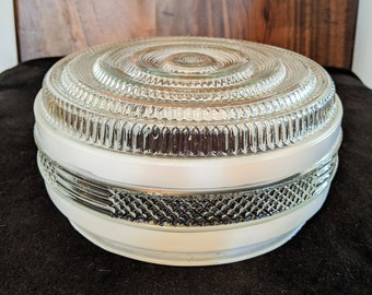 May include: A white glass ceiling light fixture with a clear, textured glass dome. The dome has a series of concentric rings and a decorative pattern around the edge.