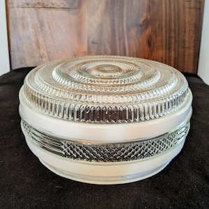 May include: A white glass ceiling light fitting with a clear, textured glass dome. The dome has a series of concentric rings and a decorative pattern around the edge.