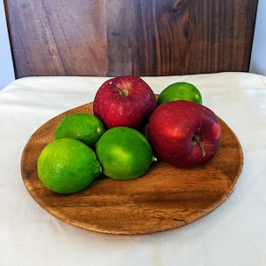 May include: A wooden serving bowl filled with red apples and green limes. The bowl is on a white tablecloth.