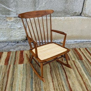 May include: A wooden rocking chair with a woven cane seat. The chair has a dark brown finish and a simple, classic design.