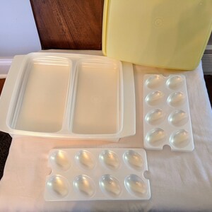 Op de afbeelding: Een set van drie witte plastic containers voor het bewaren van voedsel. De grootste container heeft twee compartimenten en de andere twee containers hebben een rooster van kleine compartimenten.