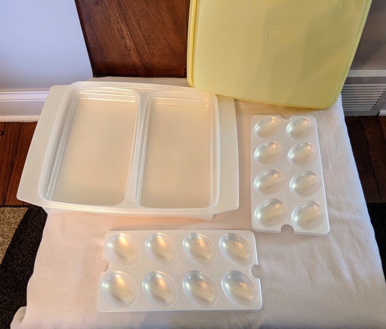 Op de afbeelding: Een set van drie witte plastic containers voor het bewaren van voedsel. De grootste container heeft twee compartimenten en de andere twee containers hebben een rooster van kleine compartimenten.