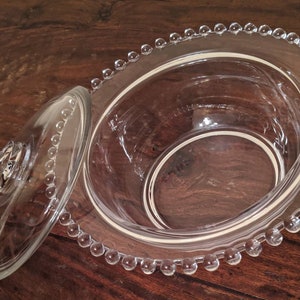 Puede incluir: Un plato de servir de vidrio transparente con un borde de cuentas y una tapa a juego. El plato est&aacute; vac&iacute;o y listo para llenarse de golosinas.