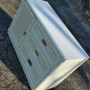 May include: White wicker cabinet with two drawers and a door. The cabinet has a white painted finish and brass hardware.