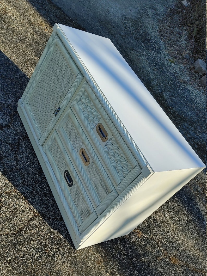 May include: White wicker cabinet with two drawers and a door. The cabinet has a white painted finish and brass hardware.