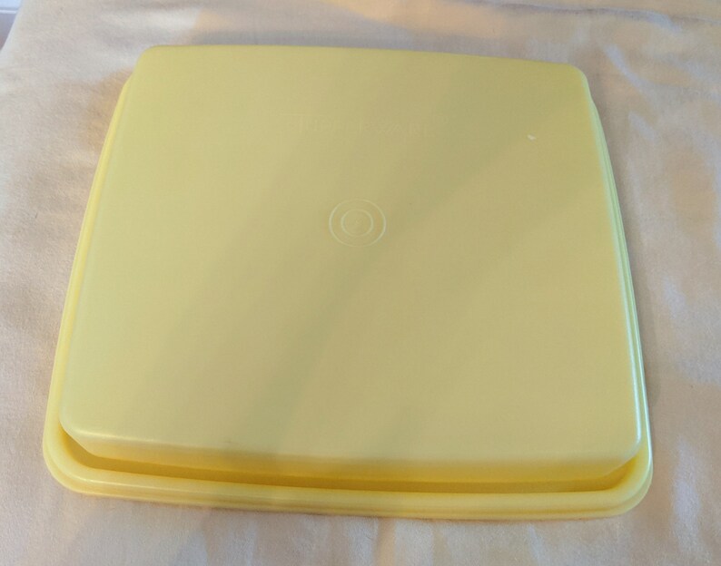 Op de afbeelding: Een rechthoekige bakvorm van geel plastic met een afgeronde rand en een kleine cirkel in het midden.