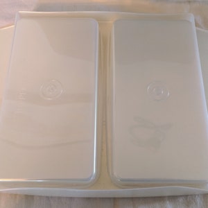Op de afbeelding: Twee transparante plastic containers met deksels, genest in een witte plastic bak. De containers hebben een cirkelvormig ontwerp aan de bovenkant.