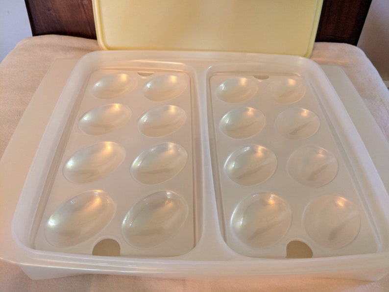 Op de afbeelding: Een witte plastic eierenopslagcontainer met een deksel. De container heeft twee rijen met zes eivormige compartimenten.