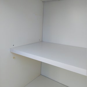 May include: A white shelf unit with a single shelf. The shelf is empty and the unit is made of white wood.