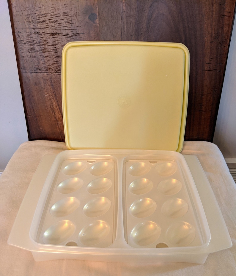 Op de afbeelding: Een transparante plastic eierdoos met een geel deksel. De doos heeft twee secties, elk met zes individuele vakken voor het bewaren van eieren.