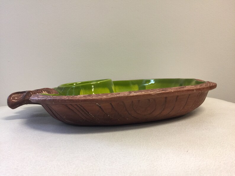 Puede incluir: Un plato de servir de cer&aacute;mica marr&oacute;n con un glaseado verde. El plato tiene una textura tallada de madera y un peque&ntilde;o taz&oacute;n redondo para salsas.