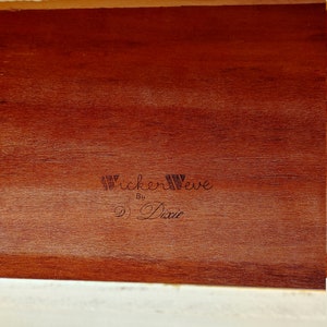 May include: Close-up of a wooden drawer interior with a brown wood grain finish. The drawer is labeled "Wickerweave by Dixie" in black lettering.