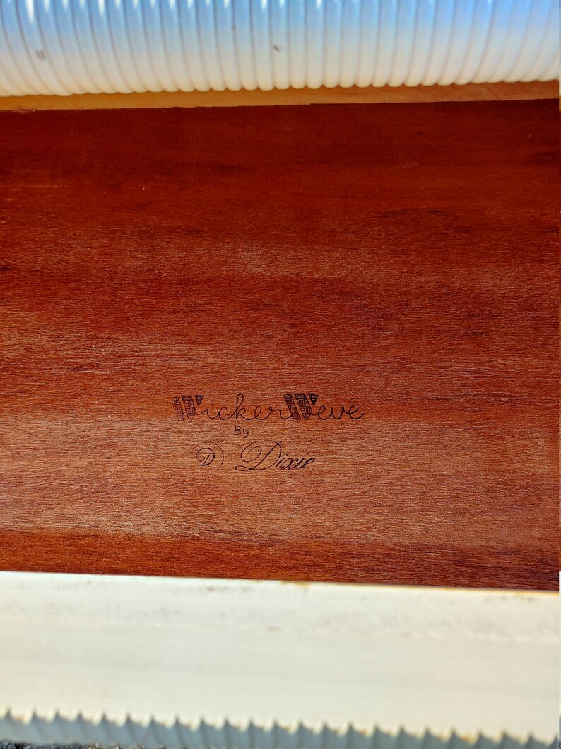 May include: Close-up of a wooden drawer interior with a brown wood grain finish. The drawer is labeled "Wickerweave by Dixie" in black lettering.