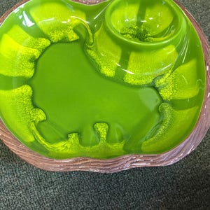 Puede incluir: Un plato de servir de cer&aacute;mica verde con un taz&oacute;n m&aacute;s peque&ntilde;o en el centro. El plato tiene un borde marr&oacute;n texturizado y un acabado verde brillante.