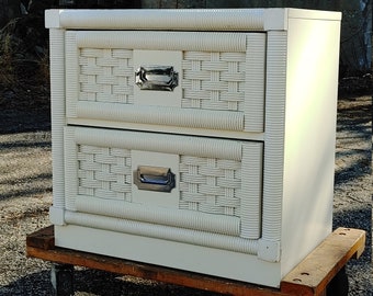 May include: Off-white two-drawer nightstand with woven drawer fronts and silver-toned handles. The nightstand is on a wooden dolly with wheels. The nightstand is a vintage style piece.