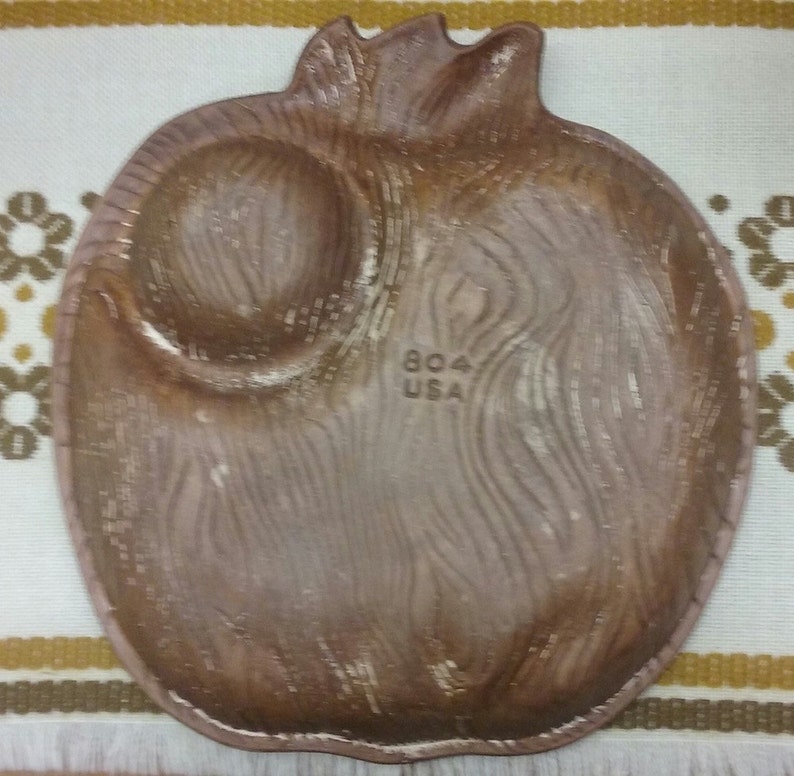 Puede incluir: Un plato de cer&aacute;mica marr&oacute;n con forma de granada con una peque&ntilde;a hendidura redonda. El plato tiene un patr&oacute;n de veta de madera y las palabras "804 USA" est&aacute;n impresas en la parte inferior.