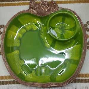 Puede incluir: Un plato de servir de cer&aacute;mica verde en forma de manzana con un taz&oacute;n m&aacute;s peque&ntilde;o adjunto. El plato tiene un tallo marr&oacute;n y una superficie texturizada.