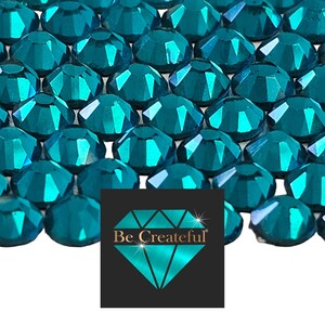 May include: A close-up image of teal blue rhinestones. The rhinestones are faceted and have a metallic sheen. The rhinestones are arranged in a random pattern.