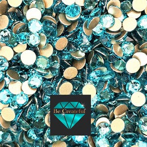 May include: A close-up image of a large quantity of turquoise blue rhinestones with silver backing. The rhinestones are scattered on a white surface. The text "Be Createful" is visible in the lower right corner of the image.